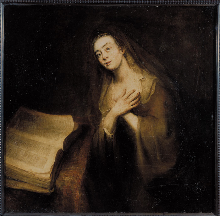 En kvinna som står invid en stor bok och håller bägge händerna framför bröstet.