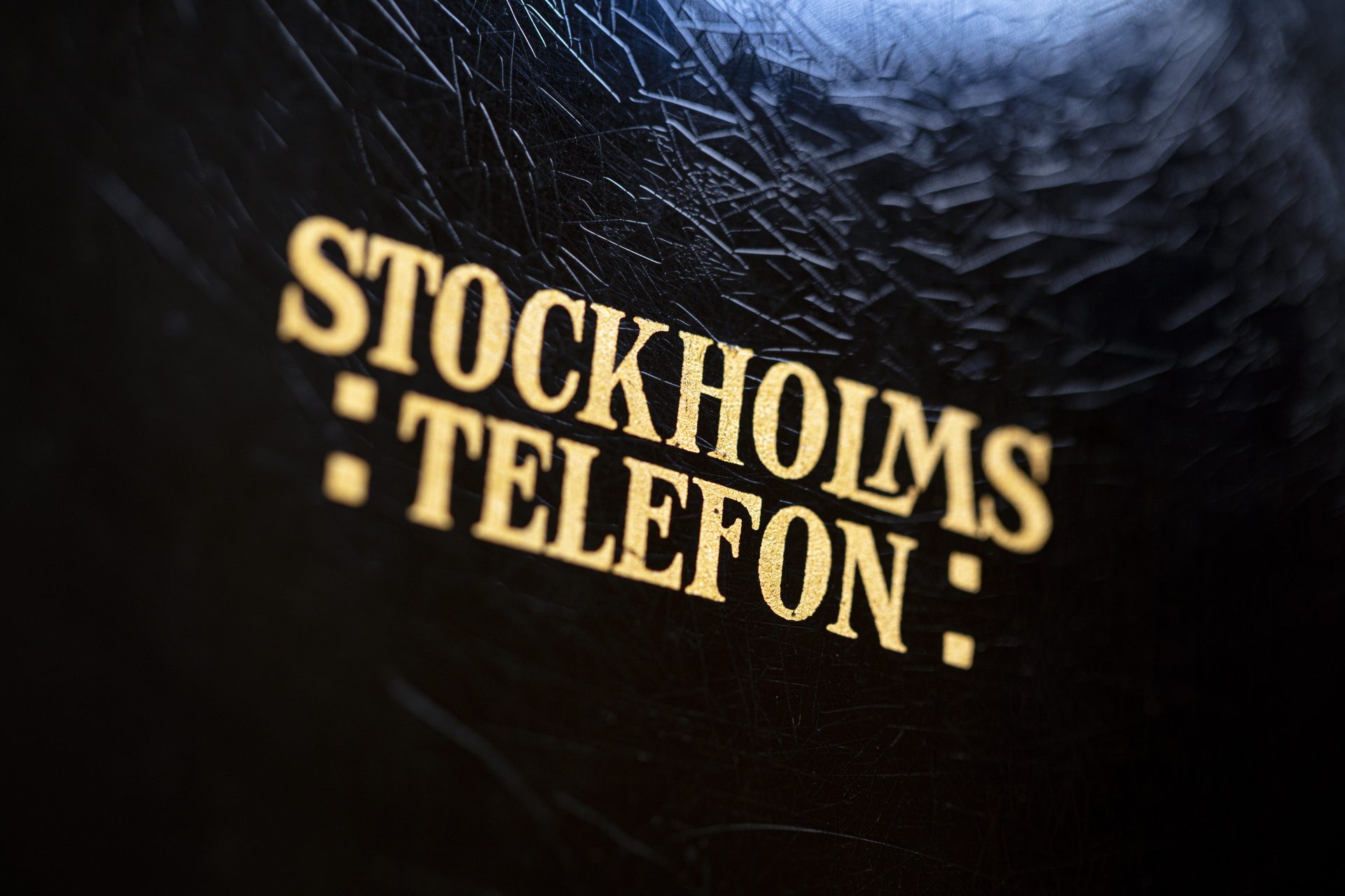 Detaljbild av texten Stockholmstelefon i guld mot svart botten.