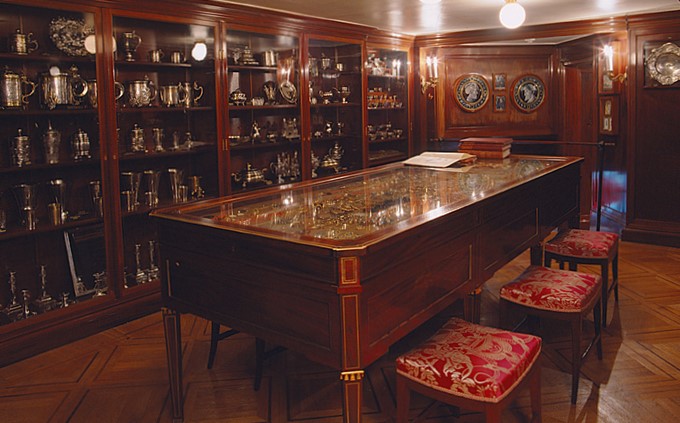 Ett rum med paneler av trä och monterskåp med glasdörrar. I mitten av rummet ett bord med glasskiva.