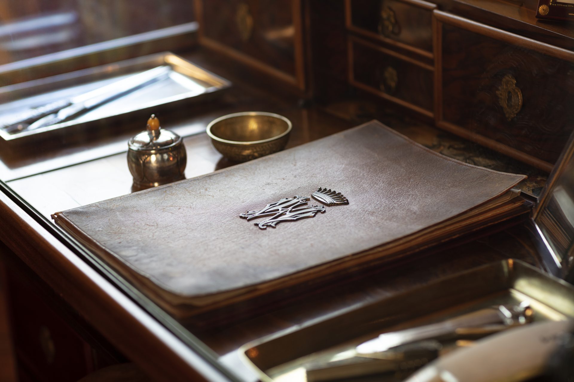 Närbild av ett skrivbord med ett bläckhorn och en läderpärm med metalldekorationer.