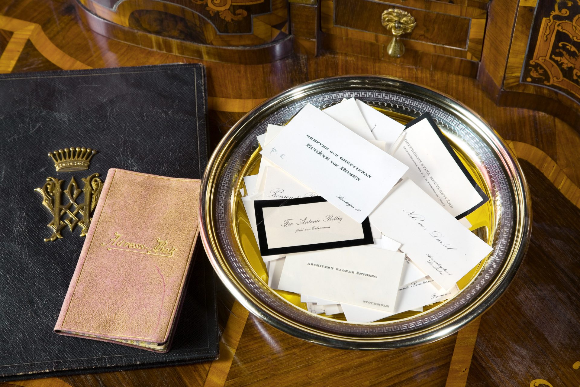 Ett silverfat med flera visitkort och bredvid en liten adressbok och en större svart brevpärm.