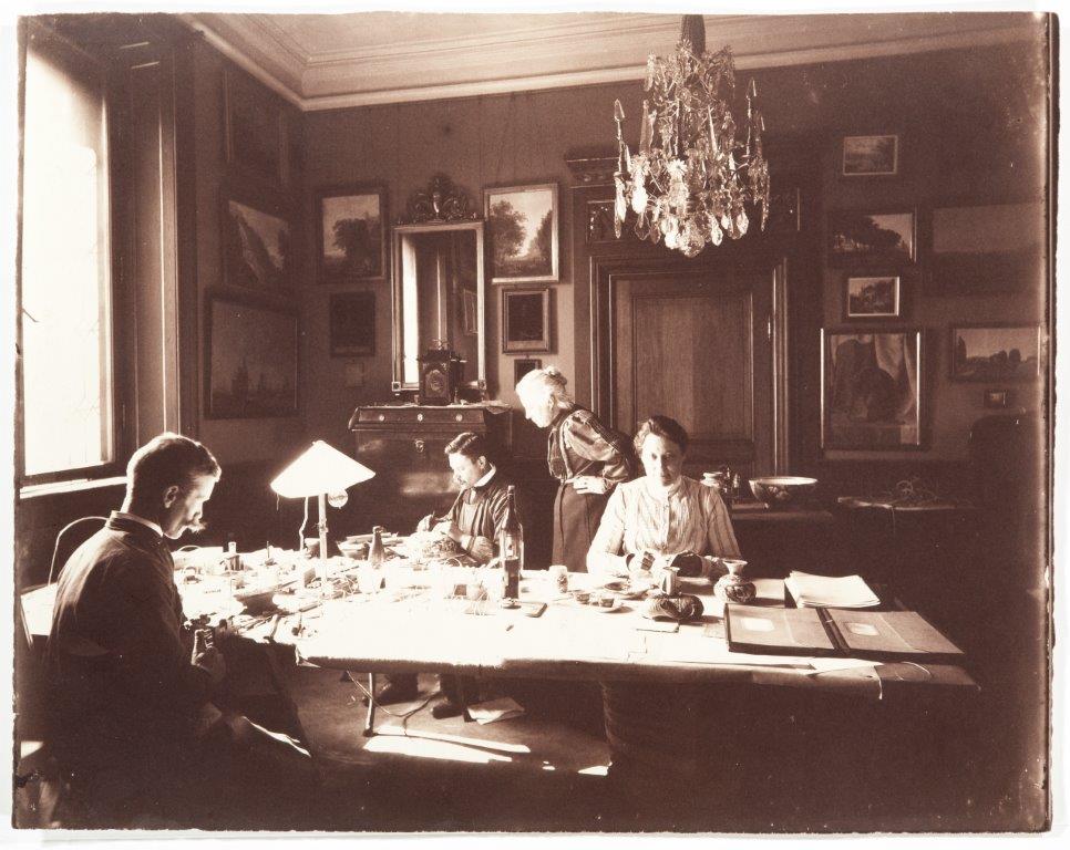 Wilhelmina von Hallwyl och några av hennes anställda sitter vid ett bord och namnger olika inventerier 