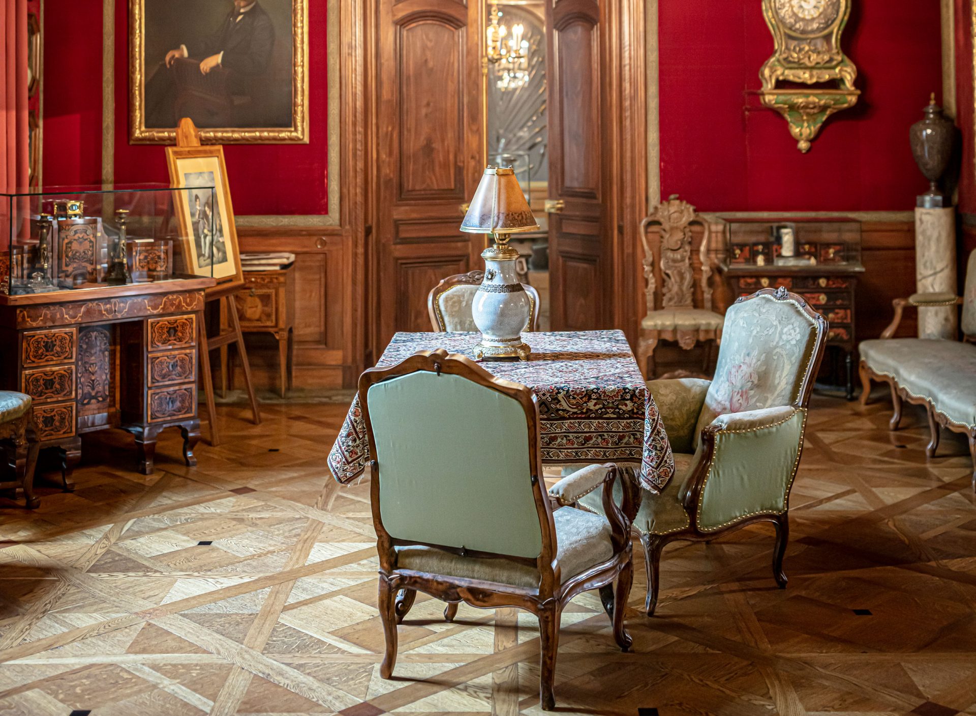 Ett rum med väggar klädda med mörkrött tyg. I mitten ett bord och stolar, en del tavlor på väggarna samt en stor ljuskrona i taket.
