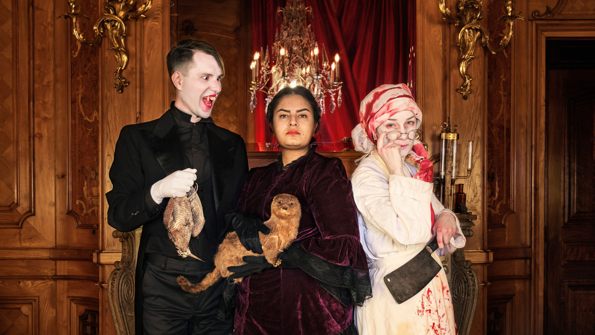 Three people standing in the museum dressed up with vampire fangs and bloody clothes.
