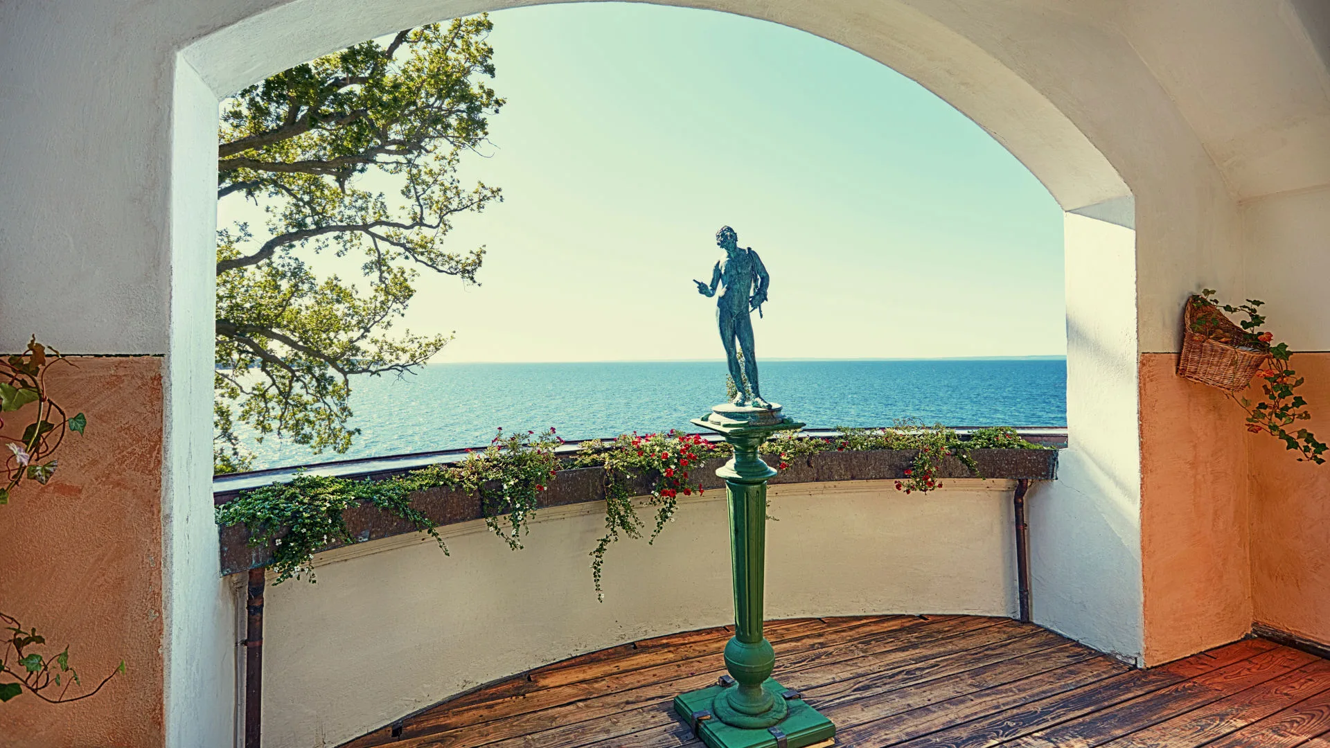 En staty som står på en balkong som vetter ut mot havet och en klarblå himel.