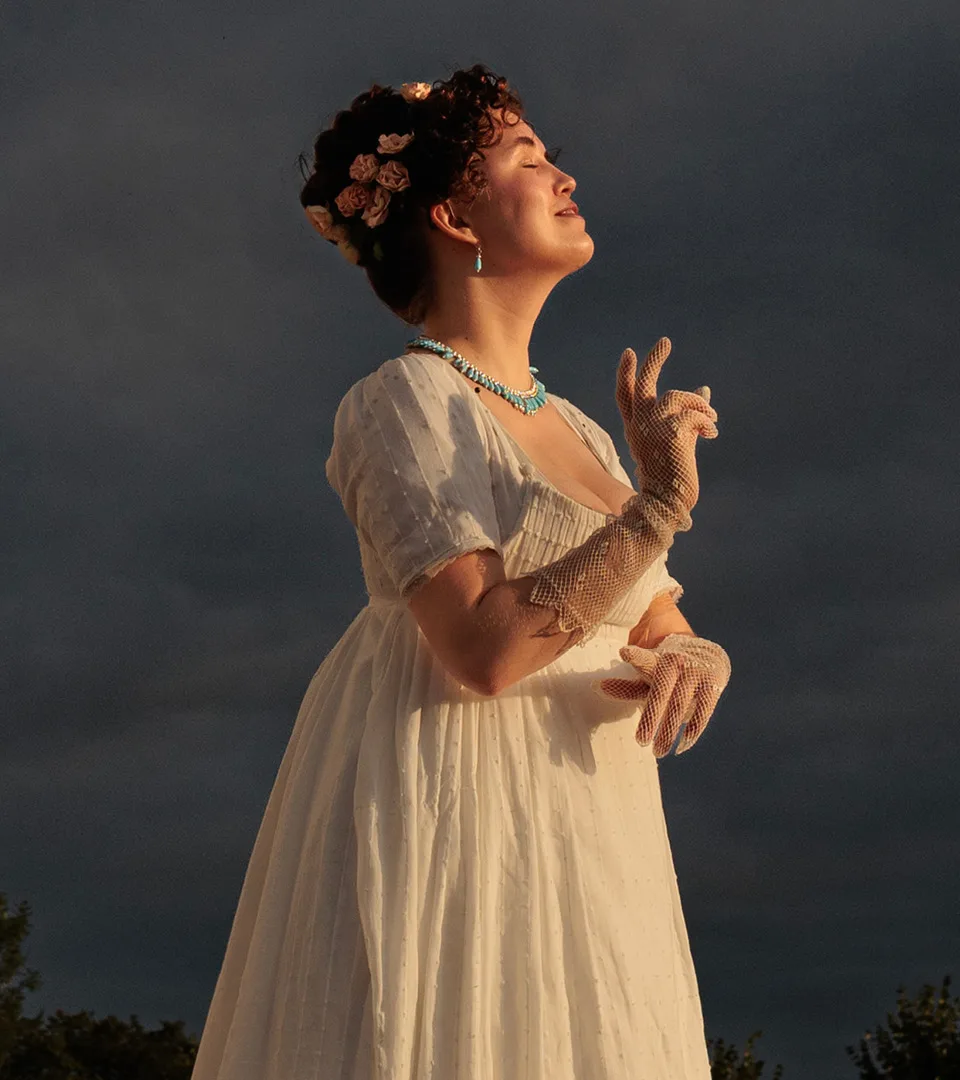 Woman with historical clothing in profile, lit up against a dark bakground