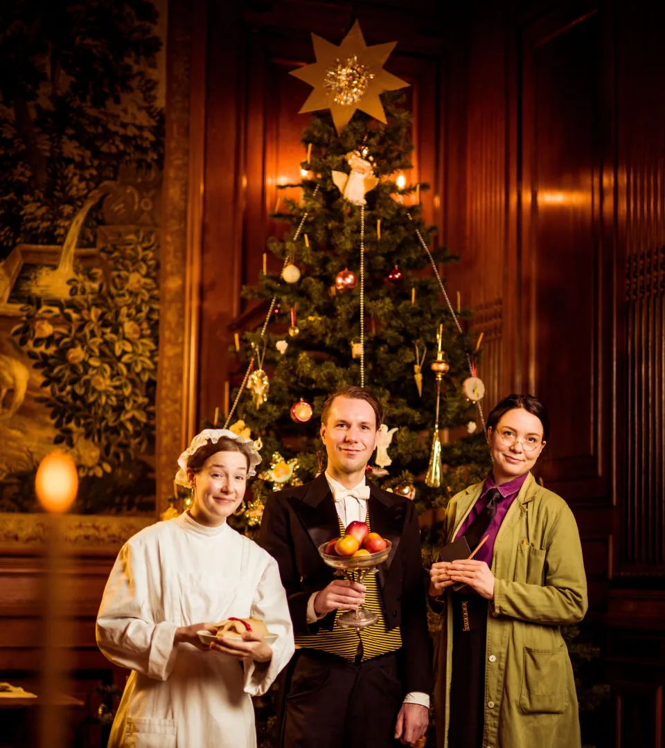 Tre personer framför en julgran i museet.